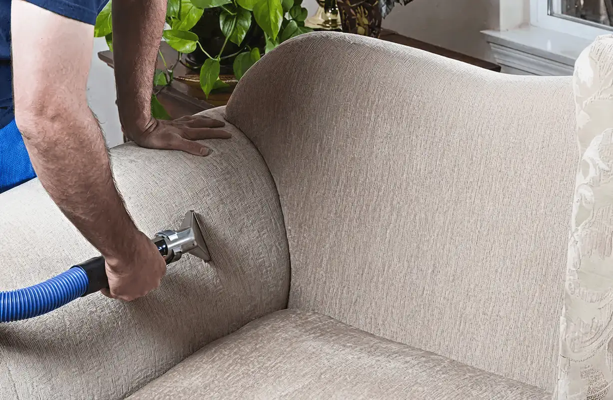 Professional upholstery cleaner deep-cleaning a fabric sofa with a handheld extraction tool and hose, Jacksonville, FL.